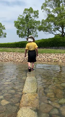 Child Walking on Stones Across Shallow Water (Vertical, Handheld)