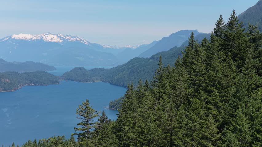 Scenic View Of A Serene Lake Surrounded By Lush Forests And Majestic Snow-Capped Mountains In British Columbia