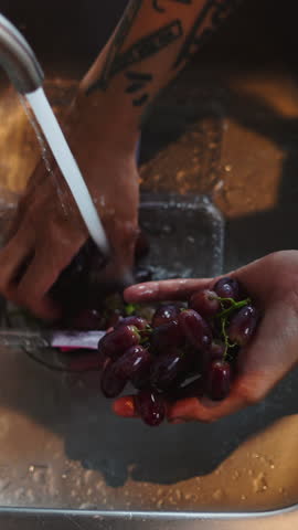 Chef carefully washes a bunch of fresh red grapes in a stainless steel kitchen sink, preparing them for a recipe