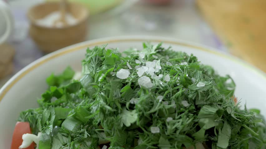Fresh parsley sprinkled with large salt crystals, topped with a drizzle of olive oil. Cook adds final touches to green salad, creating a balanced and healthy dish for family dinner