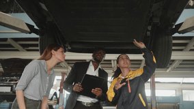 Latin mechanic manager explains to White female client and Black insured agent about EV car undercarriage fix work, claim warranty service maintenance at automotive garage, transportation industry. - Powered by Shutterstock - Get 15% off with code: PIKWIZARD15