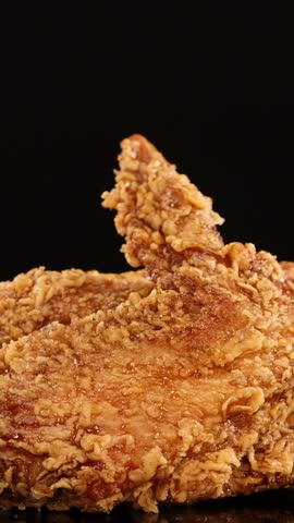 A hand reaches in and lifts a golden, crispy fried chicken wing from a pile, shot in close-up with dramatic studio lighting and a black background