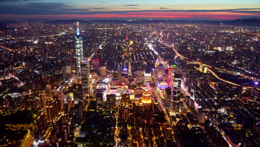 Aerial hyperlapse of Downtown Taipei at dusk, the vibrant capital city of Taiwan, with 101 Tower standing out amid skyscrapers in XinYi Commercial District and city lights dazzling under twilight sky