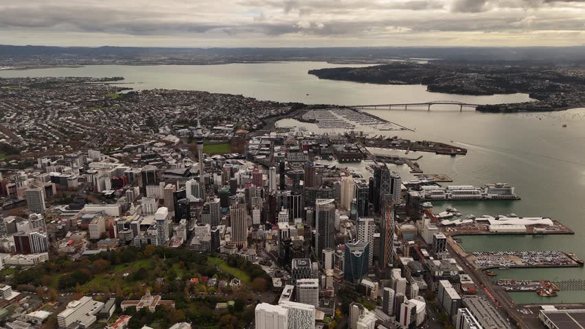 City Skyline with skyscraper in downtown of Auckland and famous Auckland Harbour Bridge in background. Aerial wide shot.
