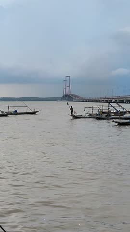 Surabaya, Indonesia - May 16, 2024, Traditional fishing boats near Suramadu Bridge in Surabaya under cloudy sky, iconic scene of Indonesian coastline