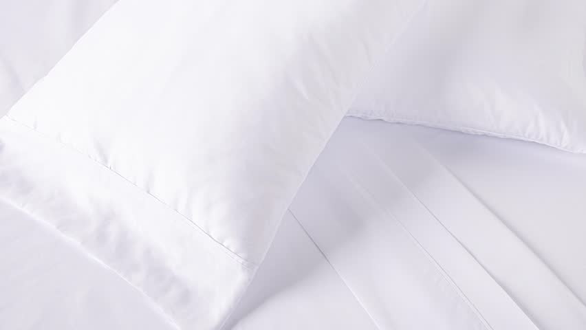 Camera slowly zooms into fresh white bedding in soft morning light