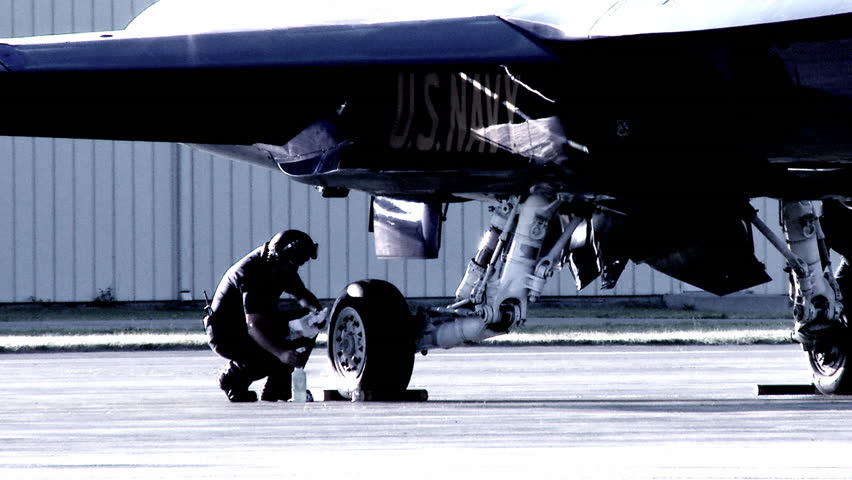 Aircrew cleaning the wheels on an F-18 Hornet fighter plane.