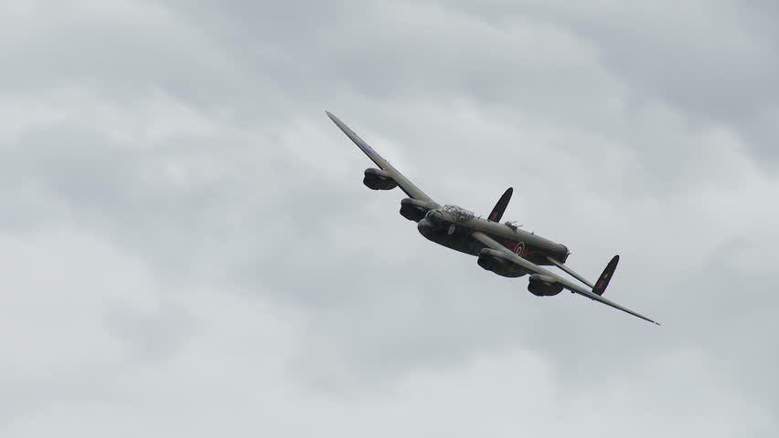 Avro Lancaster bomber plane from World War II flying past against a cloudy sky.