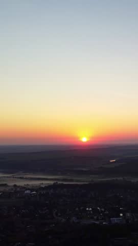 Aerial rural village in morning fog with bright sun rising over horizon on clear sky, tilt down shot