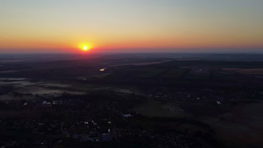 Aerial scenery of sun rising over horizon above rural village in morning fog