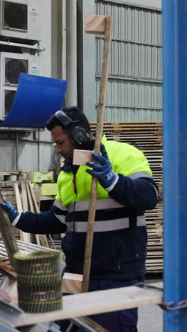 Factory worker wearing safety equipment dismantles a wooden pallet using machinery in a slow motion sequence