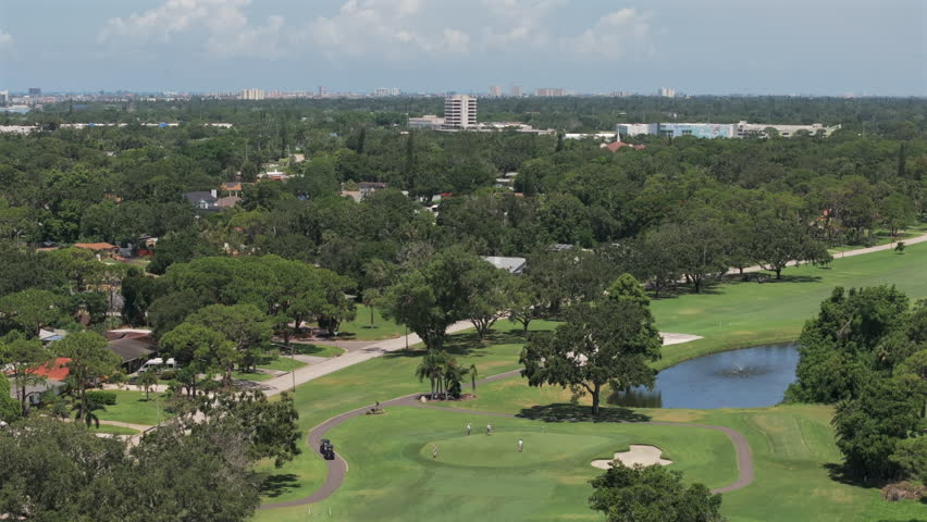 Aerial view of Florida golf course, lush fairways, nearby homes, scenic pond, coastal skyline, and blue skies—perfect blend of leisure, nature, and suburban lifestyle.
