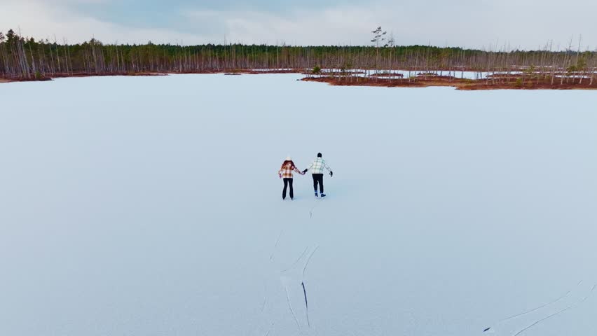 Romantic couple skating hand in hand across Cenu bog lake in slow motion Latvia