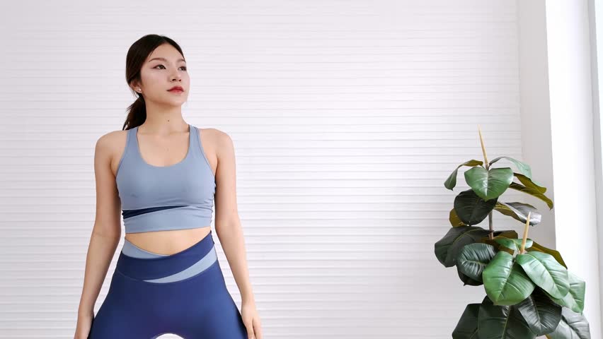 Zoom out a young woman doing a yoga side stretch on a pink mat in a bright studio with city view. Wellness, flexibility, fitness, mindfulness through daily yoga practice, healthy lifestyle. 4k video