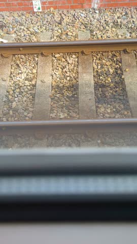 Vertical Video of Railway Tracks Whilst at Station. Public Transportation Footage on British Rail Network. Wooden Sleepers Supporting Hot Rolled Steel for Carriage to Ride On.