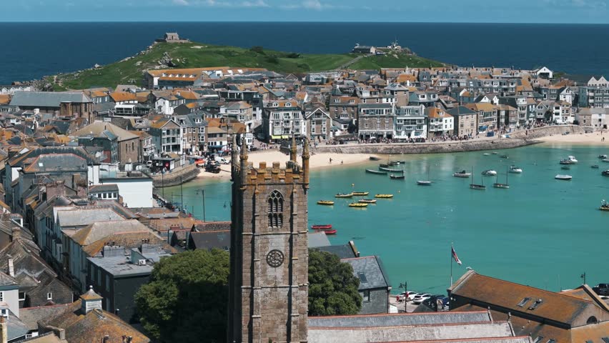 Dolly right over St Ives church with boats and bay in the distance beneath blue sky