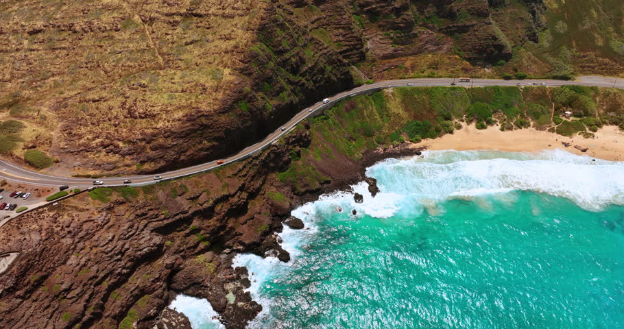 Cars go by the highway passing the spectacular rocks. Turquoise water and foamy waves roll to the sandy beach. Top view.
