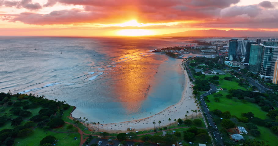 Amazing sunset over the ocean waterscape. Sky, clouds and water colored orange. Footage above the green shore of Honolulu, Hawaii, USA. Aerial view.