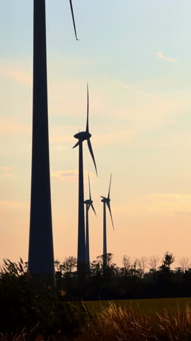 Wind turbines silhouettes at the backdrop of sky at sunset. Low angle view at the wind mills producing green energy. Vertical video.