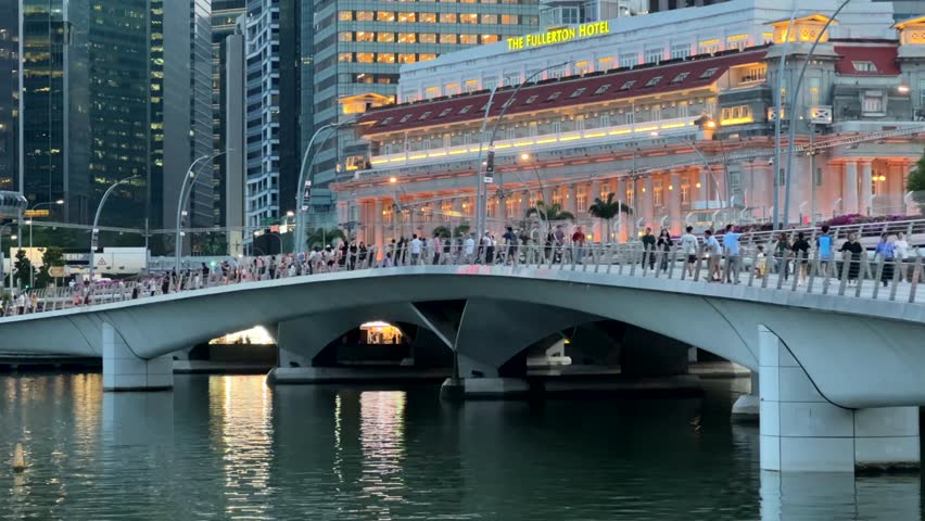 SINGAPORE, SINGAPORE - 25th SEPTEMBER 2024: Static clip of Jubilee Bridge and Fullerton hotel as tour boat passes under bridge on a beautiful evening