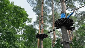 Brave girl navigating a challenging high-ropes course, balancing on wooden steps high among the pine trees.Child in a safety helmet and harness conquers an obstacle in a treetop adventure park - Powered by Shutterstock - Get 15% off with code: PIKWIZARD15