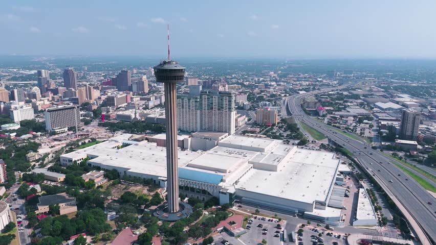The Hemisfair Tower, also known as the Tower of Americas, sits in the heart of downtown San Antonio Texas surrounded by tall buildings, crowded highways and bustling city life.