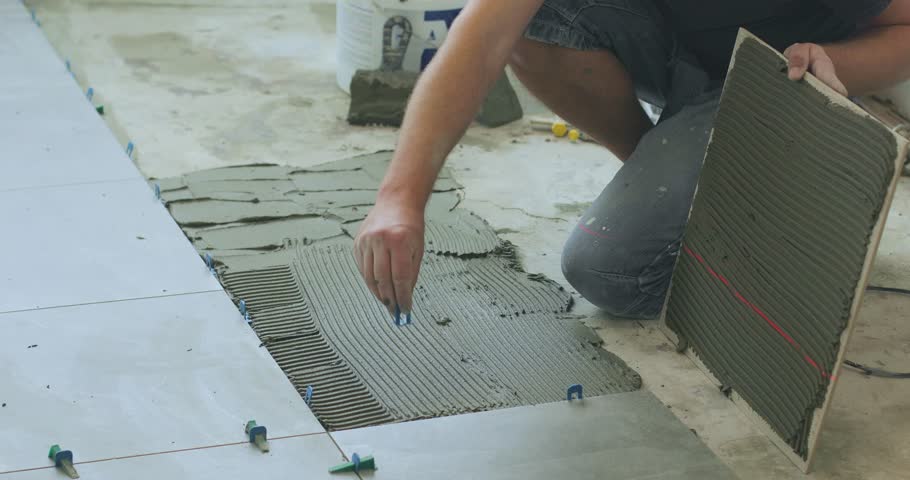 A tiler lays ceramic or porcelain tiles on the floor of a room. A man is laying tile on a floor. Room floor tile installation. Handyman laying tile.