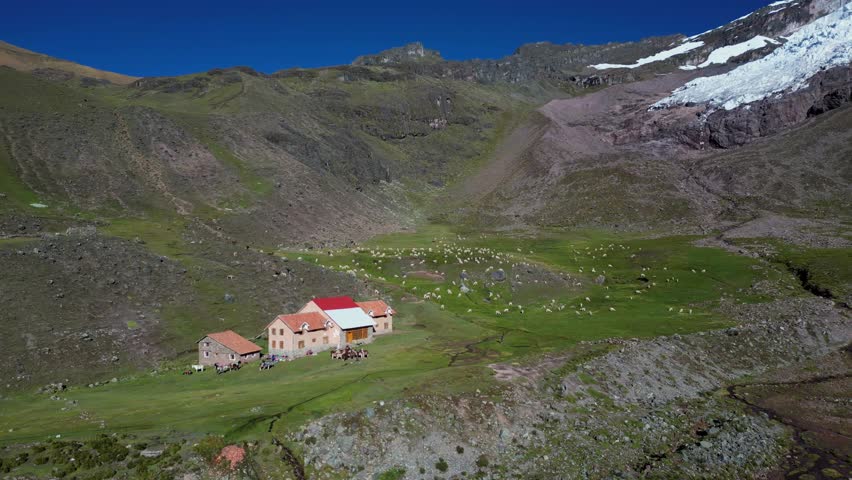 4K aerial footage of a lodge at the foot of Ausangate in the Peruvian Andes. Snowy peaks, grazing llamas, and remote wilderness create a breathtaking setting.