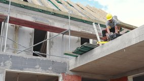 A construction worker carefully installs roofing materials on a newly built building under a clear sky. Safety measures are in place with scaffolding and gear. - Powered by Shutterstock - Get 15% off with code: PIKWIZARD15