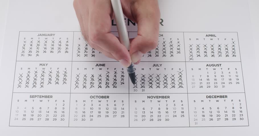 Close-up of a hand marking dates on a yearly calendar with a pen, signifying time management, planning, and organization. Person Marking Dates on Yearly Calendar with Pen