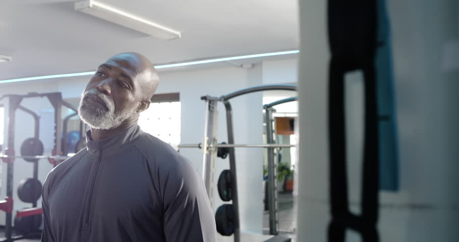Senior African American man scanning squat rack in gym, crossing chest and exuding confidence. Fitness, strength, determination, wellness, vitality, workout, contemporary