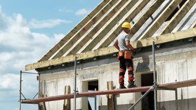 Skilled worker oversees roof assembly on a construction site, showcasing safety measures and teamwork. Bright sky enhances the active work environment. - Powered by Shutterstock - Get 15% off with code: PIKWIZARD15