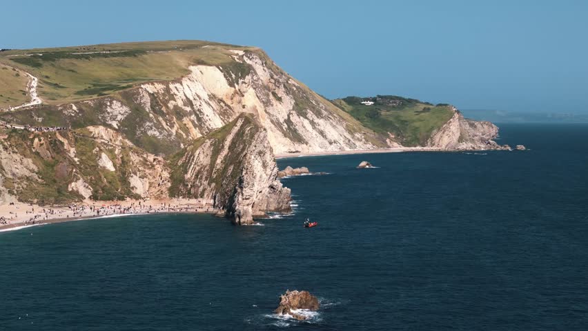 Circle left around Durdle Door with cliffs and green fields above