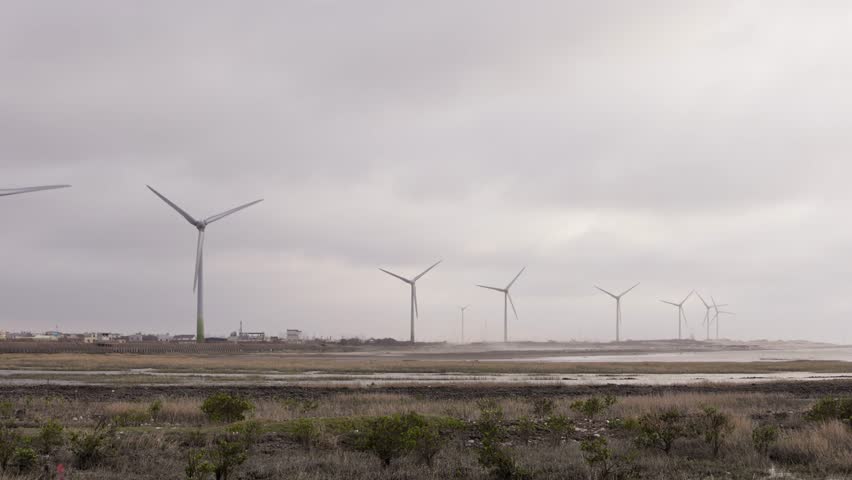 Wind turbines rotating along coastal landscape under cloudy skies. Scene of clean wind power as a renewable resource and symbol of eco friendly energy solutions.