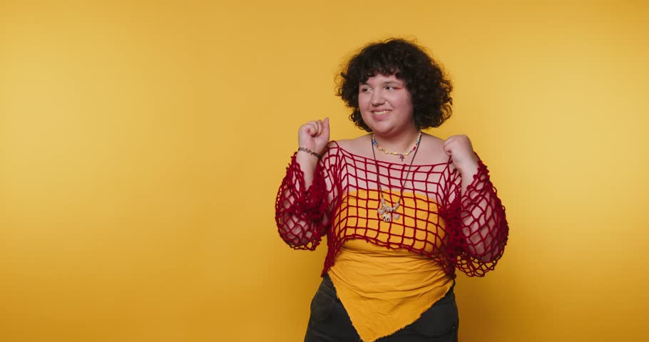 Individual dancing joyfully in front of a vibrant yellow background showcasing colorful fashion in an upbeat atmosphere shows a thumbs up and smiles