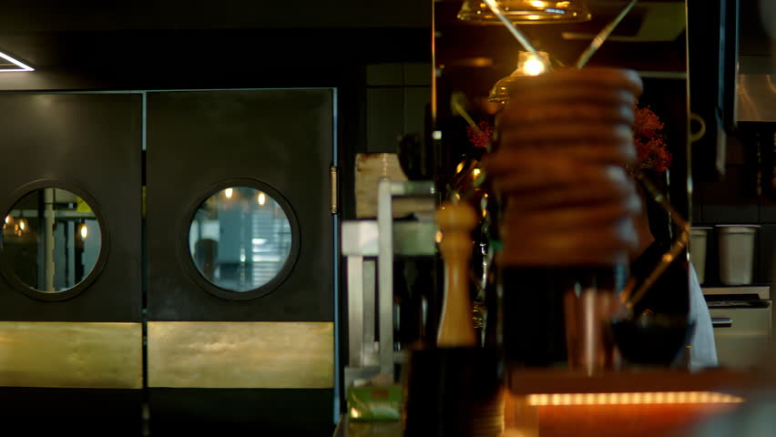 TRACKING Caucasian male chef walking out of commercial restaurant kitchen through the swinging doors. Shot with 2x anamorphic lens