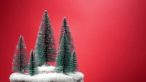 A cluster of small snow-covered bottlebrush trees rotates on a snowy base. The red background enhances the Christmas theme. - Powered by Shutterstock - Get 15% off with code: PIKWIZARD15