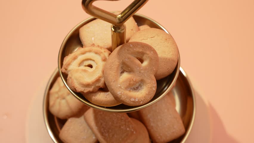 A golden tray filled with assorted butter cookies rotates smoothly. Each cookie has a unique shape and golden-brown texture.