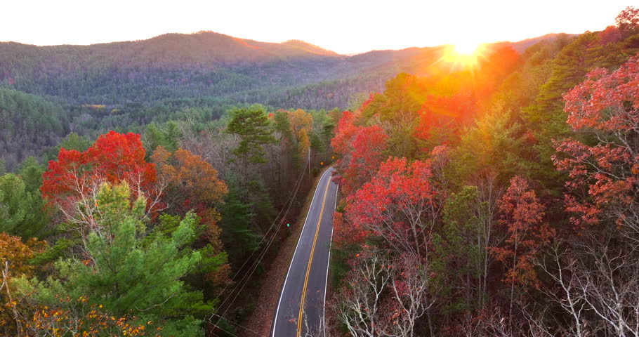 Car cruising on scenic road in Appalachian mountains at sunset. Trees glowing in vibrant fall foliage as the sun sets