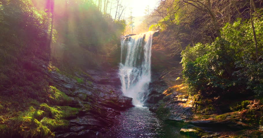Dry Falls in North Carolina. Clear water falls behind a rocky overhang, surrounded by colorful autumn trees in the Appalachian Mountains