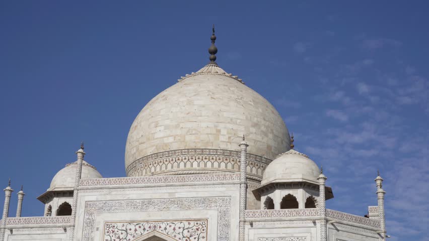 Close up shot of the main dome of the Taj Mahal showing the intricate architecture, writing, inlay work and carvings on the wall and the smaller domes against a blue sky