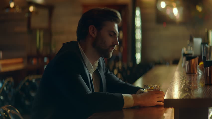 Beautiful Caucasian male sitting in a stylish restaurant, drinking cocktail. Shot with 2x anamorphic lens