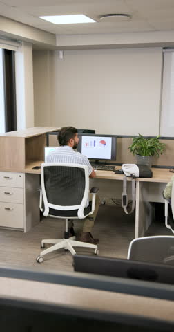 Office worker is entering cubicle reviewing charts packing laptop and plant for coworker handoff. Professional, collaborative, ergonomic, digital, workspace, organizational, vertical video