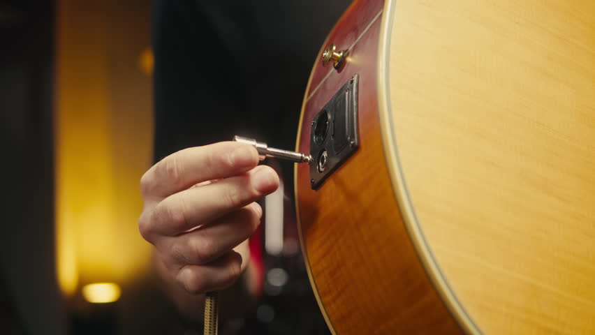 Young musician man turn on his acoustic guitar among music equipment in studio close-up. Guitarist plays melody. Playing the chords. Solo concert, music repetition