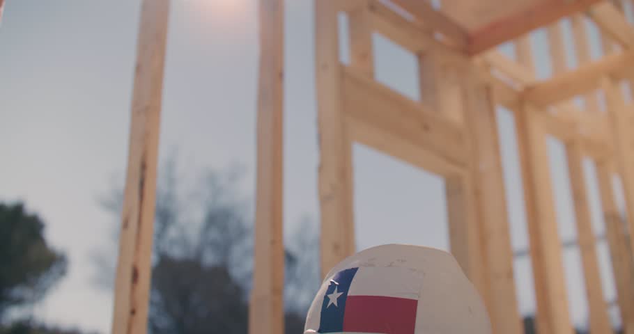 Close Up of Construction Worker Wearing Hard Hat With Texas Stickers Inside Wooden Frame of House at Construction Site