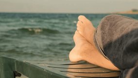 Bare male feet on a beach lounger with a view of the sea horizon. A man covered with a towel lies on the lounger watching the sea waves during sunset. - Powered by Shutterstock - Get 15% off with code: PIKWIZARD15