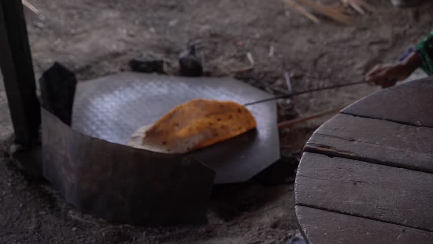 Traditional flatbread cooking on a rustic griddle over an open fire, Close-up of a person preparing traditional unleavened bread with a rolling pin on a worn wooden board, the artisanal process.