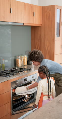 Mother and daughter in kitchen opening oven and placing hot rolls onto cooling rack for tasting. Family, baking, homestyle, kitchen, warmth, happiness, vertical video