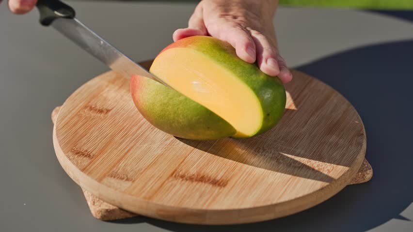 chef cuts fresh ripe mango on cutting board to prepare a healthy meal. outdoor cooking, food closeup