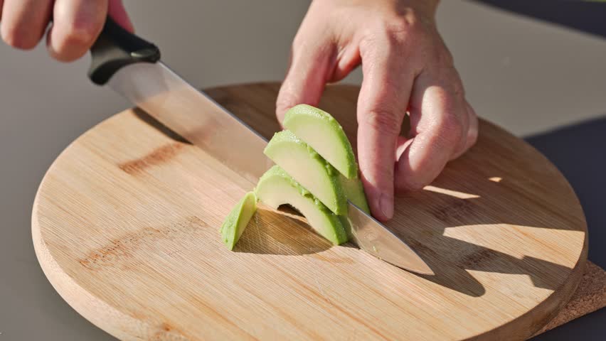 chef cuts fresh green avocado on cutting board to prepare a healthy meal. outdoor cooking, food closeup